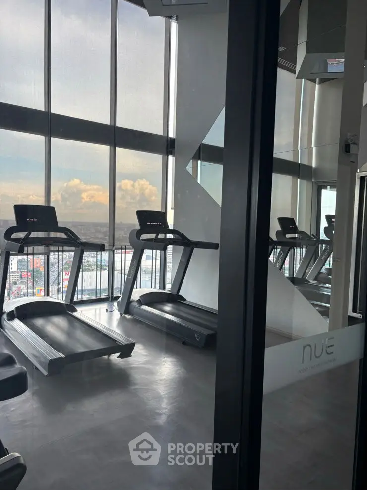 Modern gym with treadmills and panoramic city view in high-rise building.