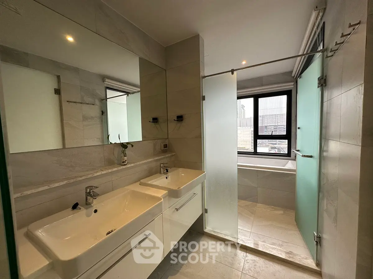 Modern bathroom with dual sinks and frosted glass shower in luxury apartment.
