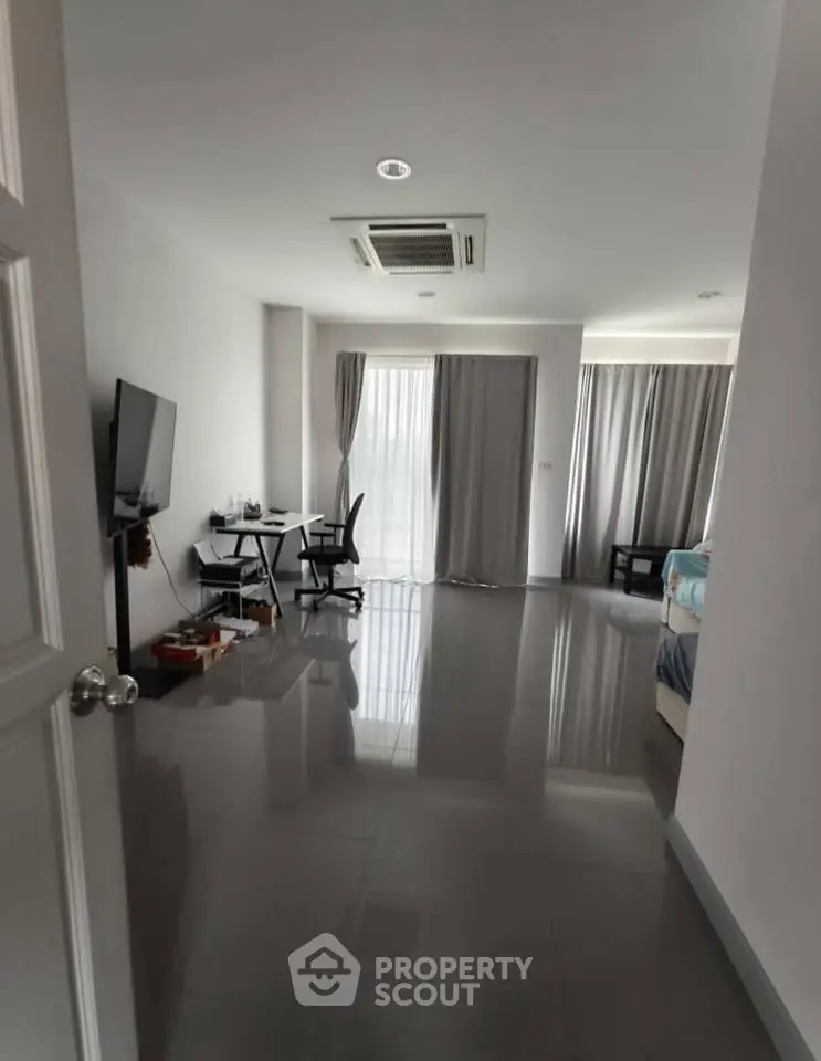 Spacious modern living area with sleek flooring and natural light, featuring a cozy workspace and entertainment setup.