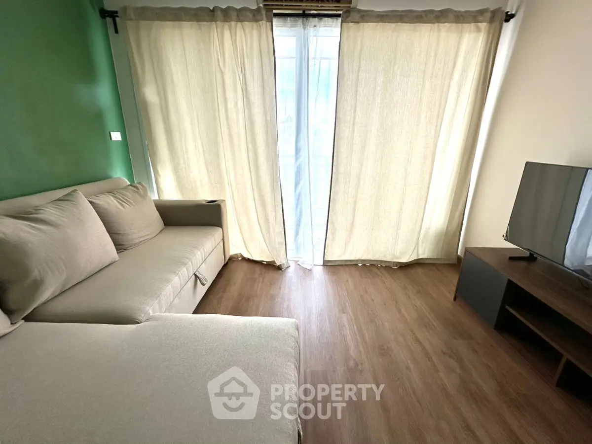 Cozy living room with modern sofa and TV, featuring natural light through large windows and elegant curtains.