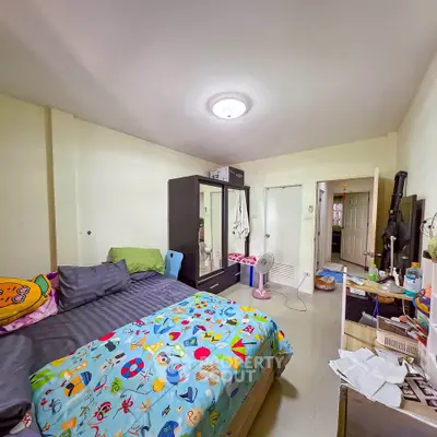 Cozy bedroom with colorful bedding and ample storage in a well-lit apartment.