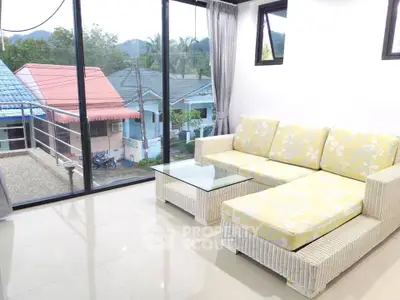 Bright living room with wicker furniture and large windows overlooking suburban homes.