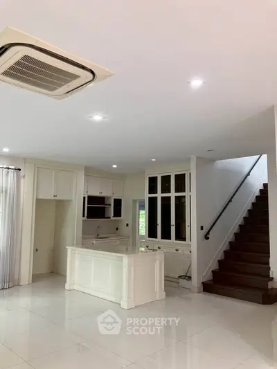 Spacious modern kitchen with white cabinetry and staircase in open layout home