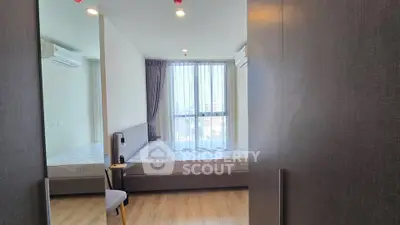 Modern bedroom with large window and city view, featuring sleek furniture and wooden flooring.