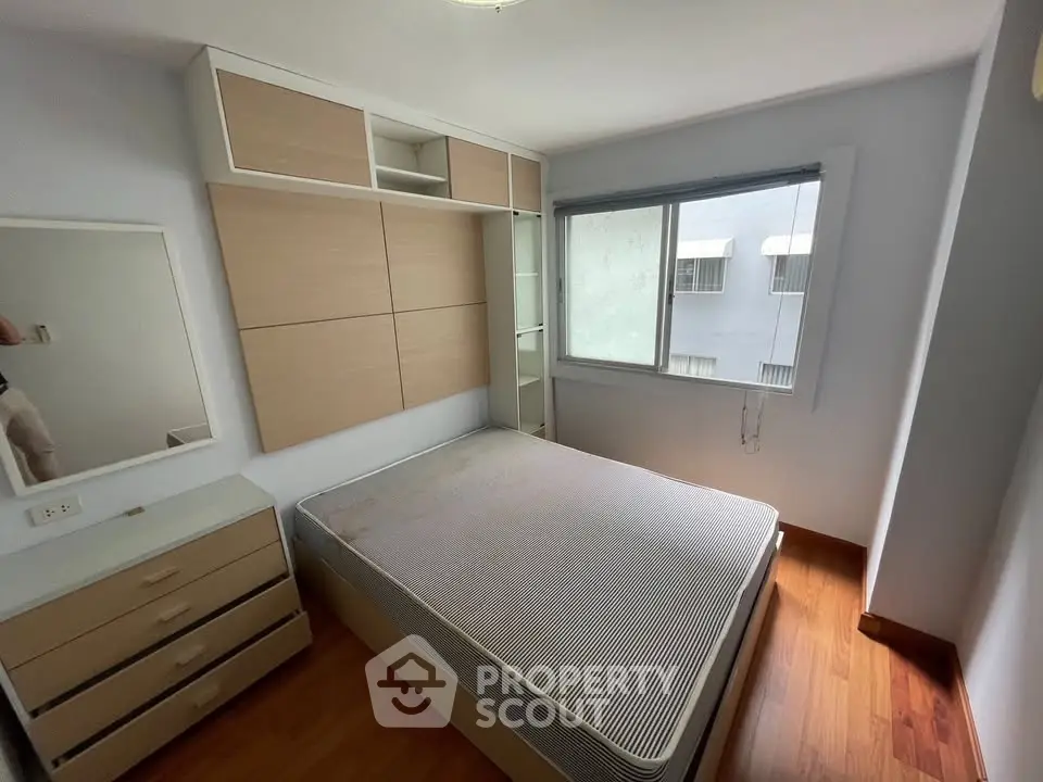 Cozy bedroom with wooden flooring and built-in storage, featuring a large window for natural light.