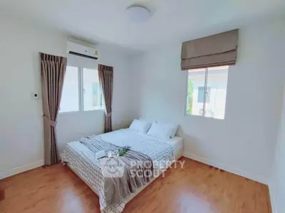 Bright and cozy bedroom with wooden flooring and large windows in modern home.