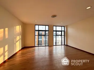 Spacious living room with gleaming hardwood floors and abundant natural light from floor-to-ceiling windows, leading to a cozy balcony.