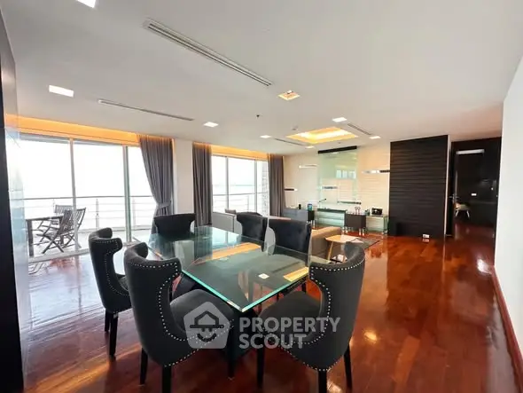 Spacious modern dining area with elegant glass table and plush chairs, featuring floor-to-ceiling windows and balcony access.