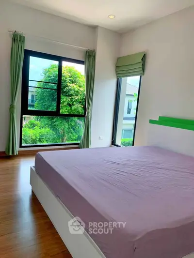Bright bedroom with large windows and green curtains offering a lush garden view.