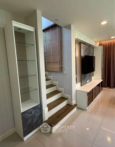 Modern living room with stylish staircase and built-in TV unit, featuring sleek design and ample natural light.