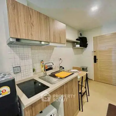 Modern compact kitchen with wooden cabinets and sleek appliances in a cozy apartment setting.