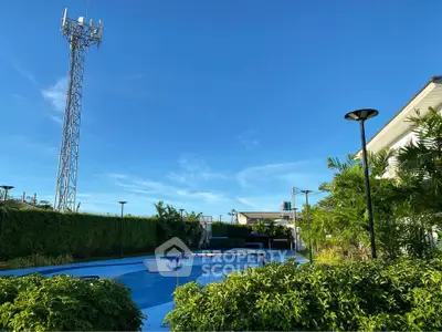 Stunning outdoor pool area with lush greenery and clear blue skies, perfect for relaxation and leisure.
