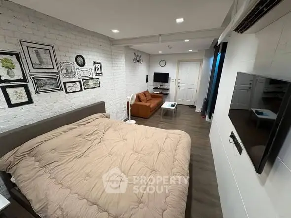 Modern studio apartment with cozy bed and stylish living area, featuring wall art and sleek furnishings.