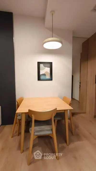 Modern dining area with wooden table and chairs, stylish pendant light, and contemporary artwork.