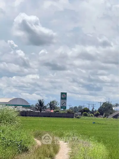 Expansive green field with distant view of buildings and signage under a cloudy sky.