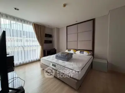 Spacious bedroom with large window and modern furnishings in a stylish apartment.