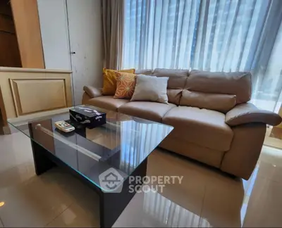 Modern living room with leather sofa and glass coffee table, featuring large windows and stylish decor.