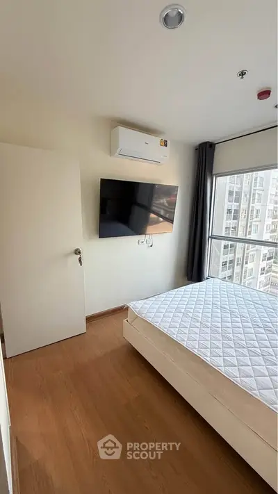 Modern bedroom with large window and wall-mounted TV in high-rise apartment.