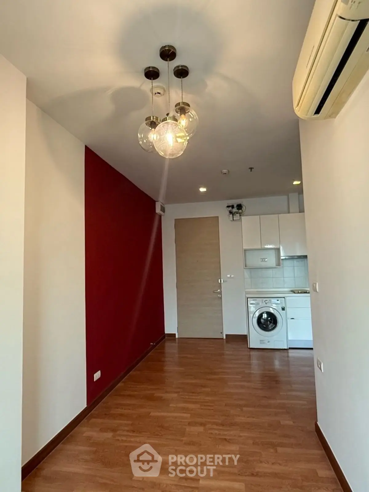 Modern apartment interior with stylish lighting and hardwood floors, featuring a compact kitchen and washing machine.