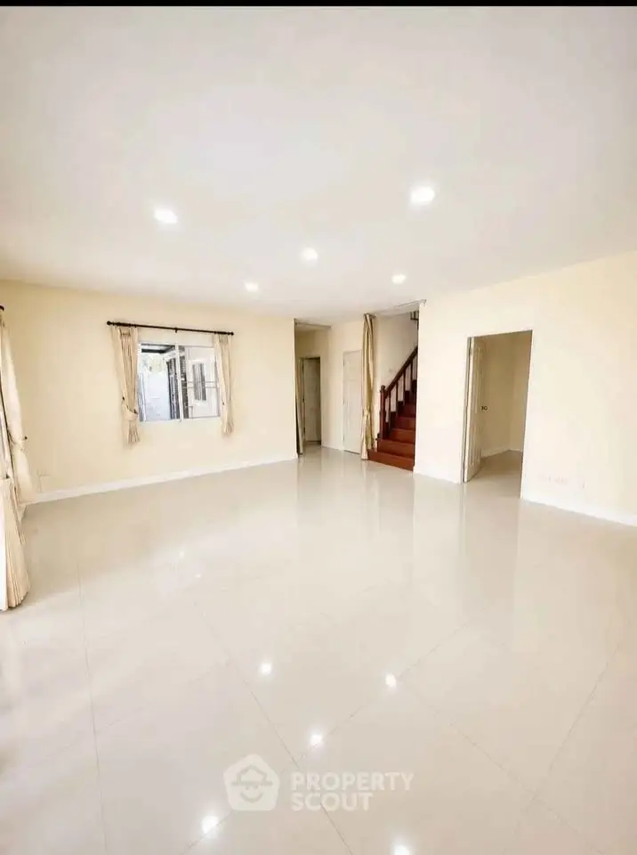 Spacious empty living room with glossy tile flooring and staircase, perfect for customization.