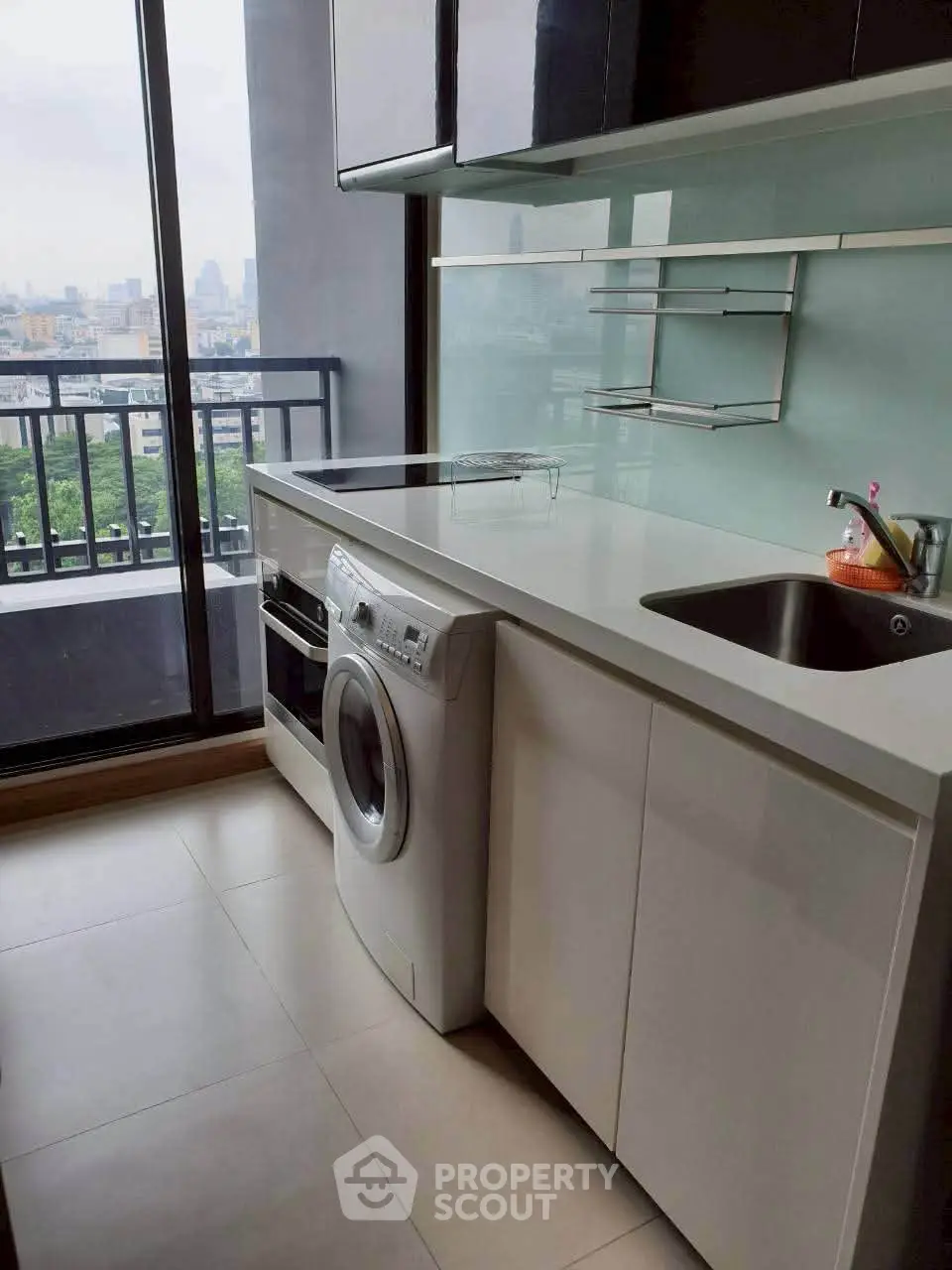 Modern kitchen with sleek cabinetry and city view from balcony, featuring built-in washing machine and oven.