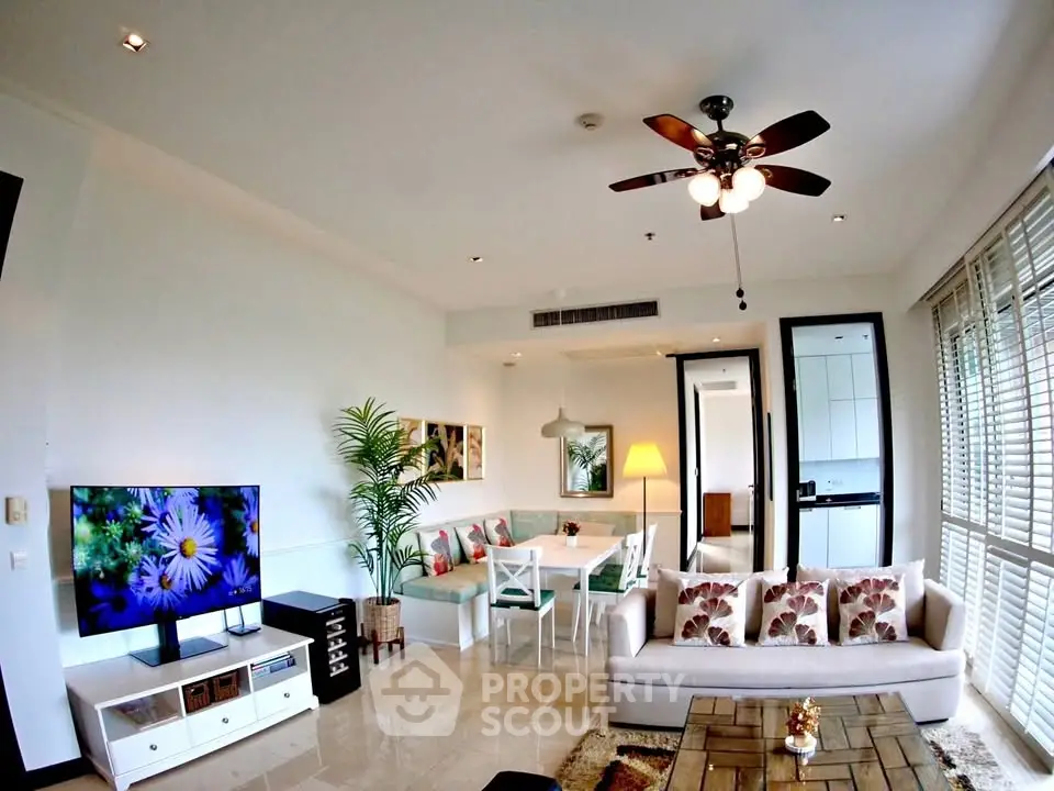 Spacious living room with modern decor and natural light, featuring a ceiling fan and large TV.