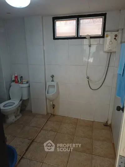 Spacious bathroom with shower and urinal, tiled walls and floor, ideal for practical living.