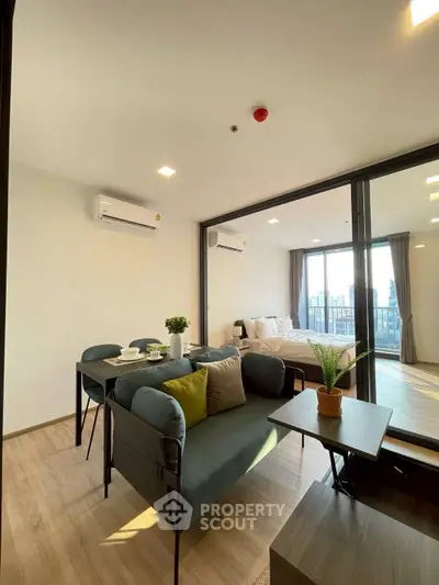 Modern open-plan living room with dining area and bedroom, featuring stylish furniture and natural light.