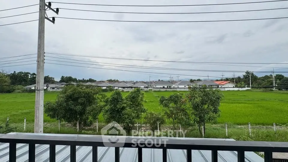 Scenic view from balcony overlooking lush green fields and distant houses.