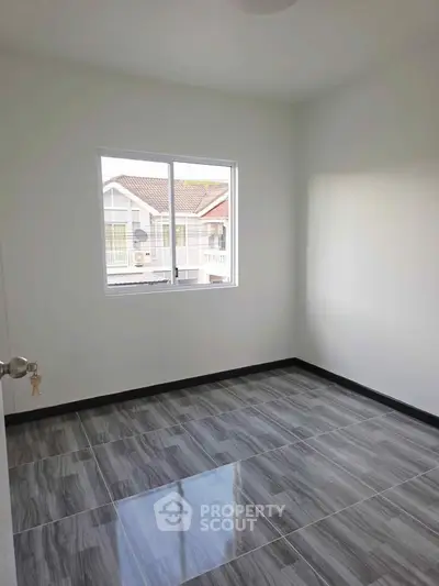 Bright empty room with large window and modern tiled flooring, perfect for customization.