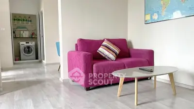 Modern living room with vibrant pink sofa and sleek glass coffee table, featuring a washing machine in the background.