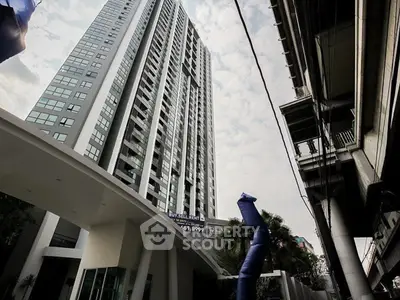 Modern high-rise building with sleek architecture and prominent for-sale banner in urban setting.