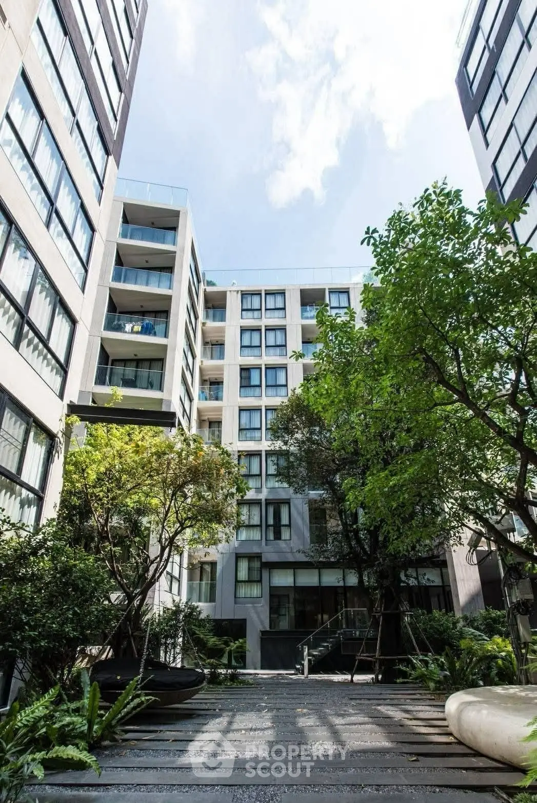 Modern apartment building with lush garden courtyard and tall windows.