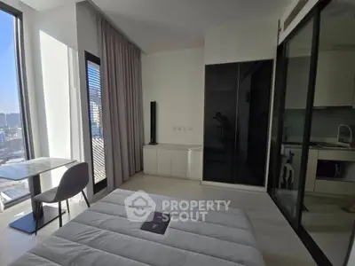 Modern bedroom with city view, sleek furniture, and adjacent kitchen area in a stylish apartment.