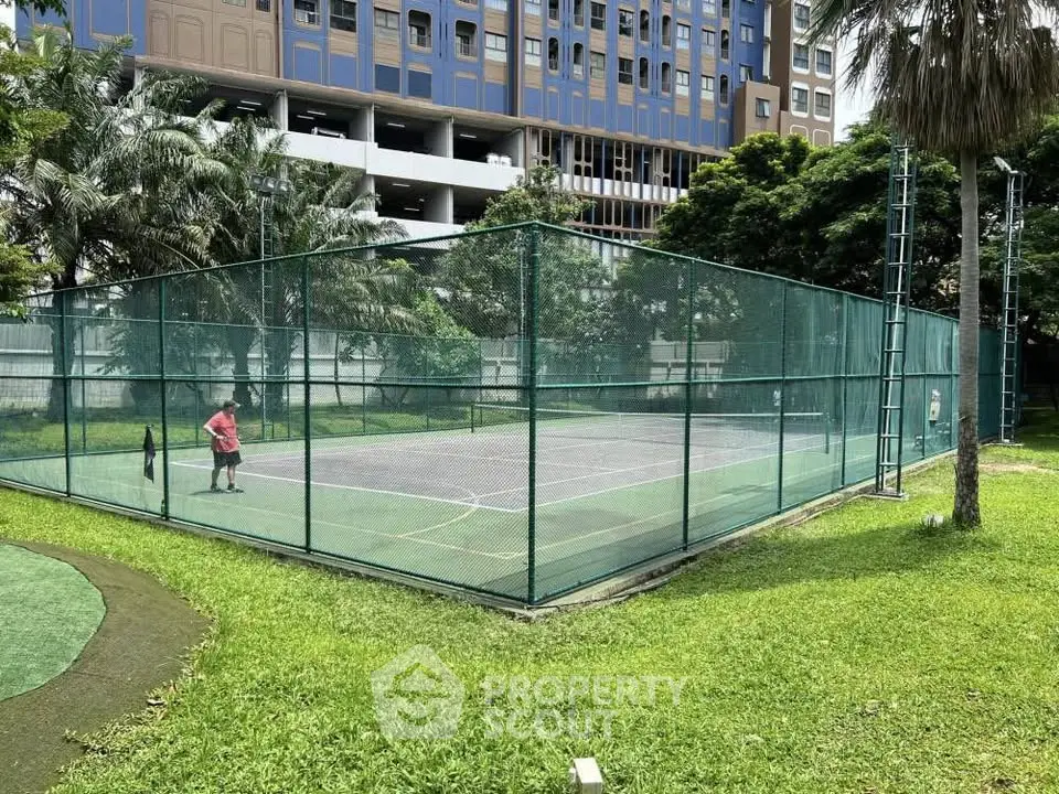 Spacious outdoor tennis court in lush green surroundings of modern residential complex.