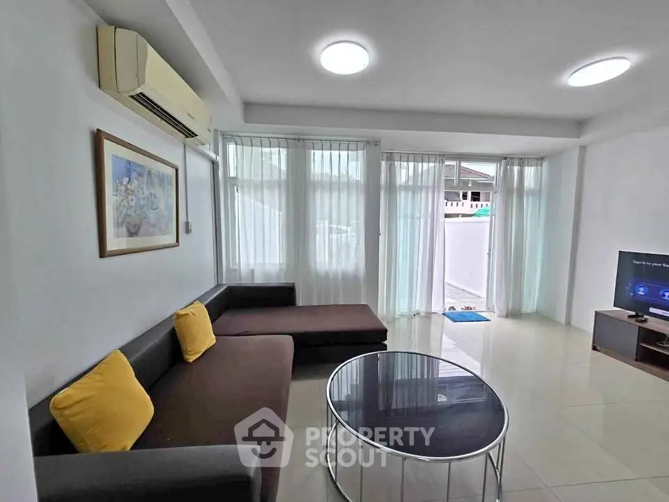 Modern living room with large windows, cozy sectional sofa, and sleek TV setup.