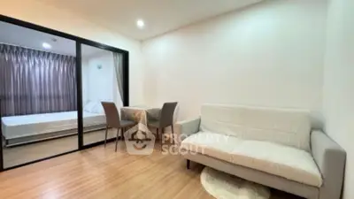 Modern living room with cozy sofa and dining area, adjacent to a bedroom with sliding glass doors.