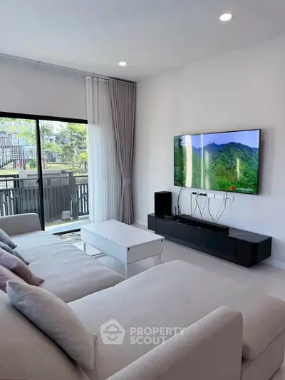 Modern living room with large TV, cozy sofa, and sliding glass doors leading to a balcony.