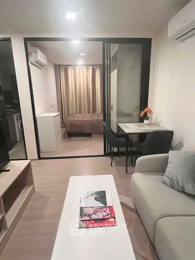 Modern living room with open layout, cozy seating, and a view into a stylish bedroom.