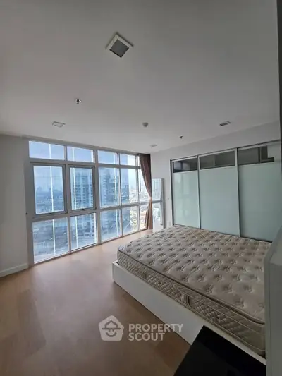 Spacious bedroom with large windows offering stunning city views in modern apartment.