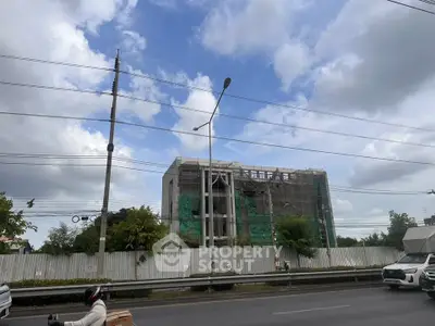 Under-construction building with scaffolding and green netting against a cloudy sky.