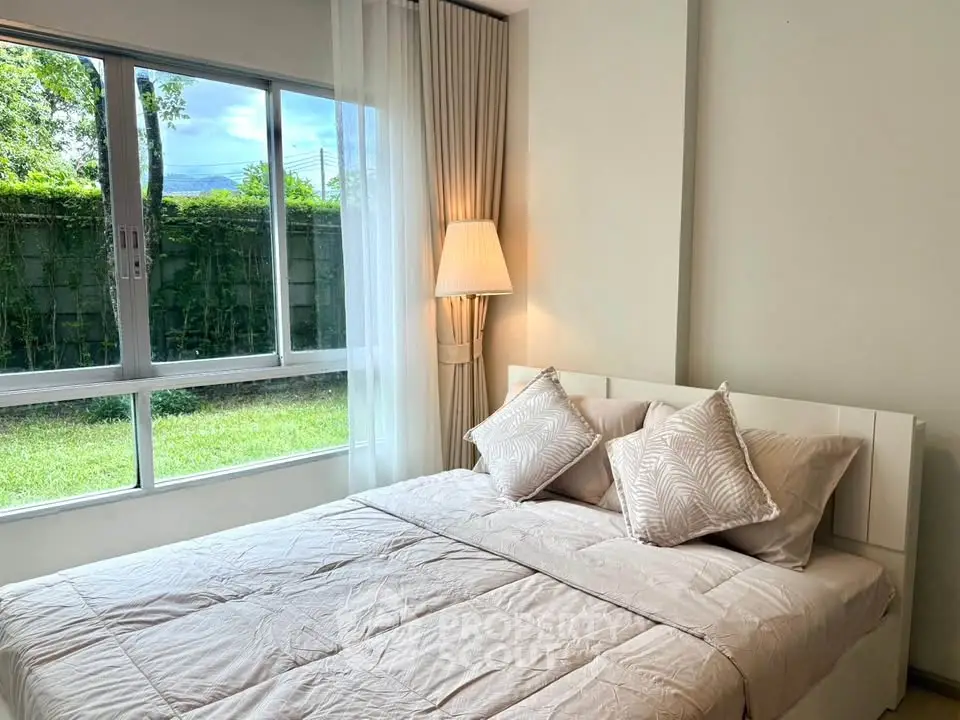 Cozy bedroom with large window overlooking lush garden, featuring elegant decor and soft lighting.