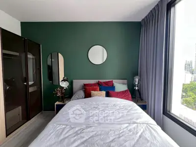 Modern bedroom with green accent wall, large window, and stylish decor in urban apartment.