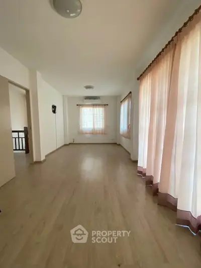 Spacious empty room with wooden flooring and large windows with curtains