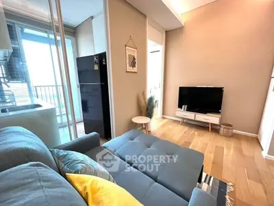 Modern living room with cozy sofa and TV, open to a balcony with natural light.