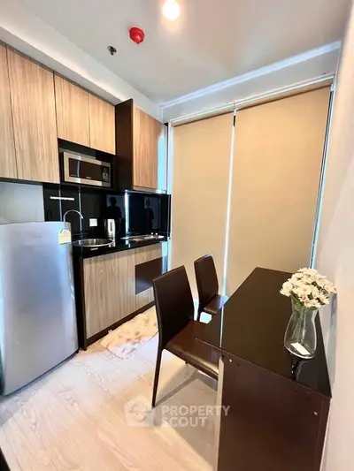 Modern kitchen with sleek cabinetry, compact dining area, and natural light from large window blinds.