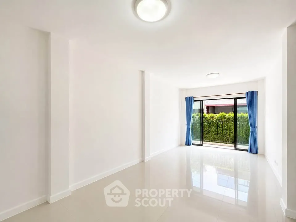 Spacious empty living room with large windows and blue curtains, overlooking a lush garden.