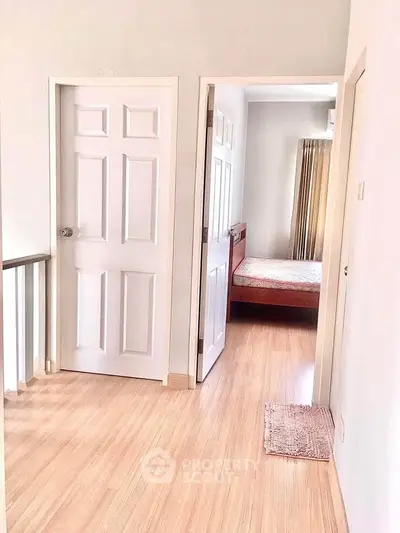 Bright hallway leading to a cozy bedroom with wooden flooring and natural light.