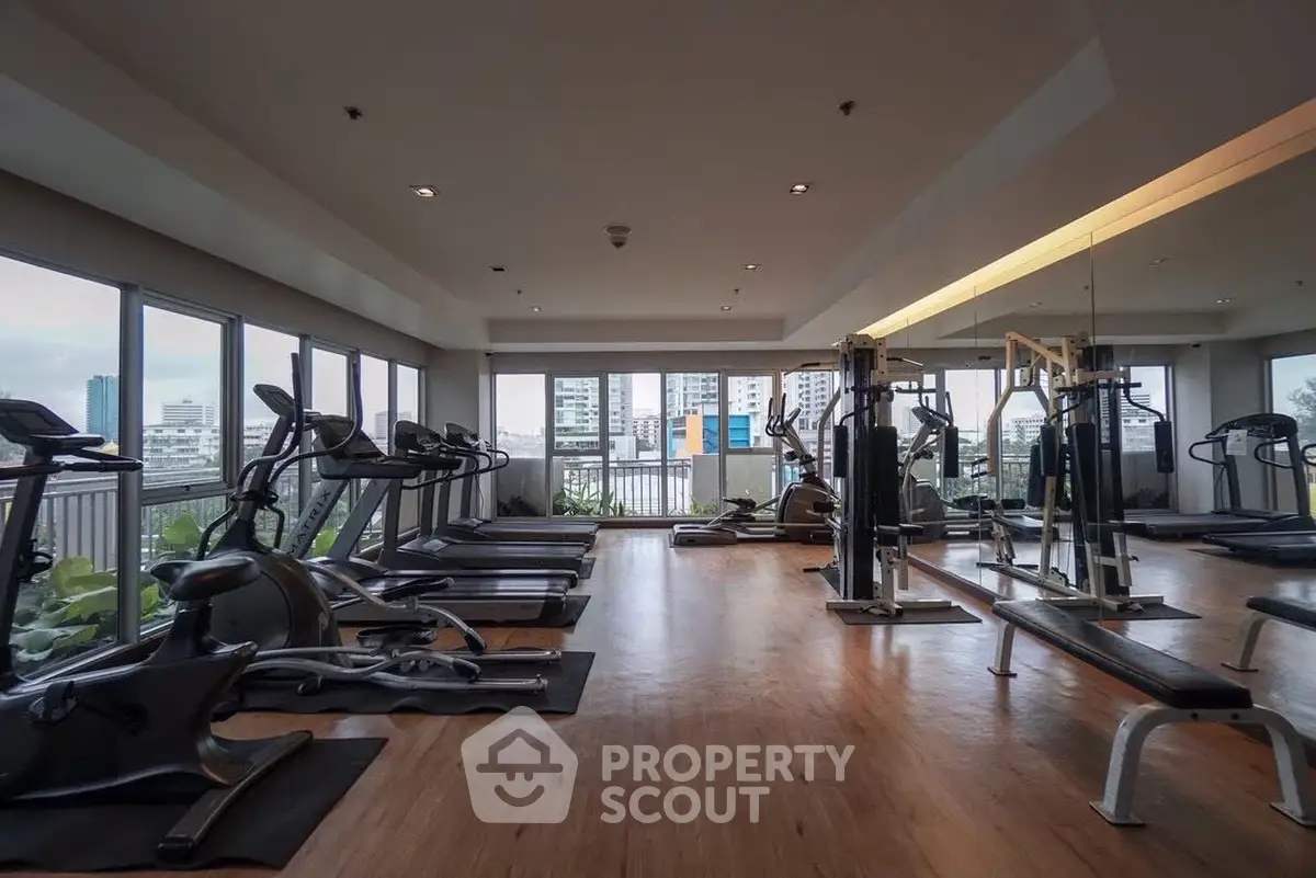 Spacious gym with modern equipment and city view in luxury apartment building.