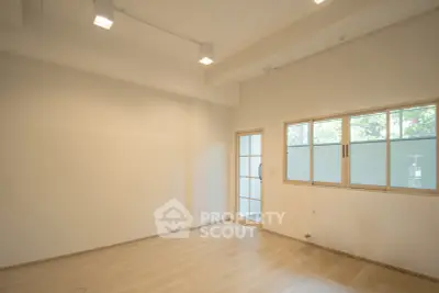 Spacious empty room with wooden flooring and large window, perfect for customization.